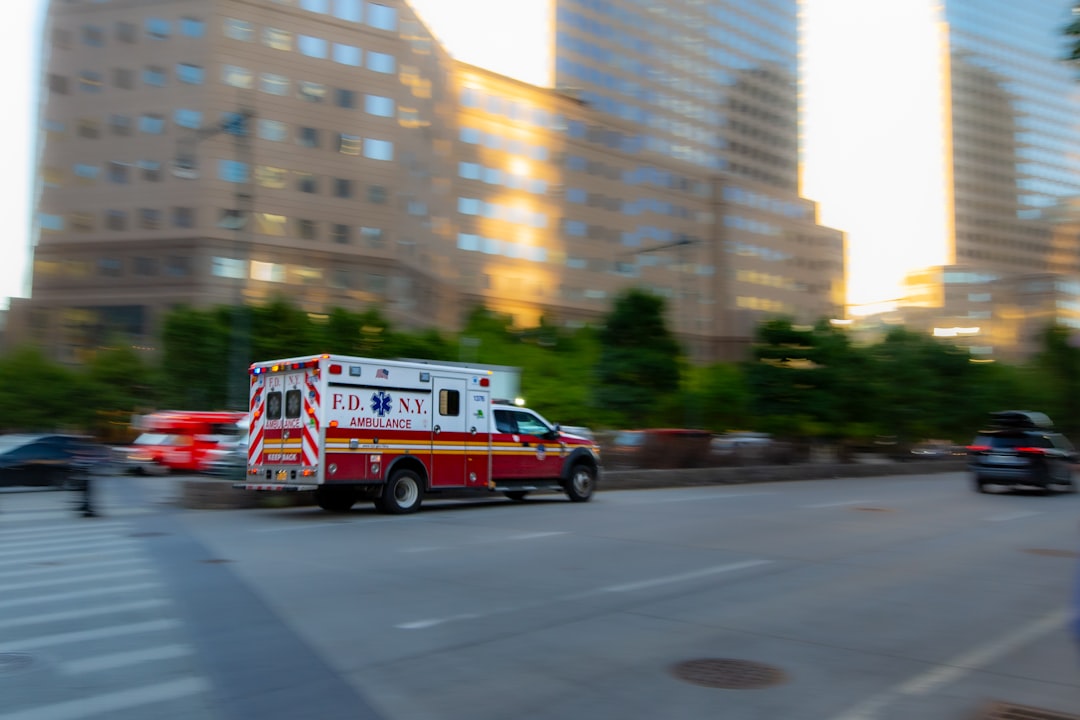 Ambulance driving on a city street with buildings.