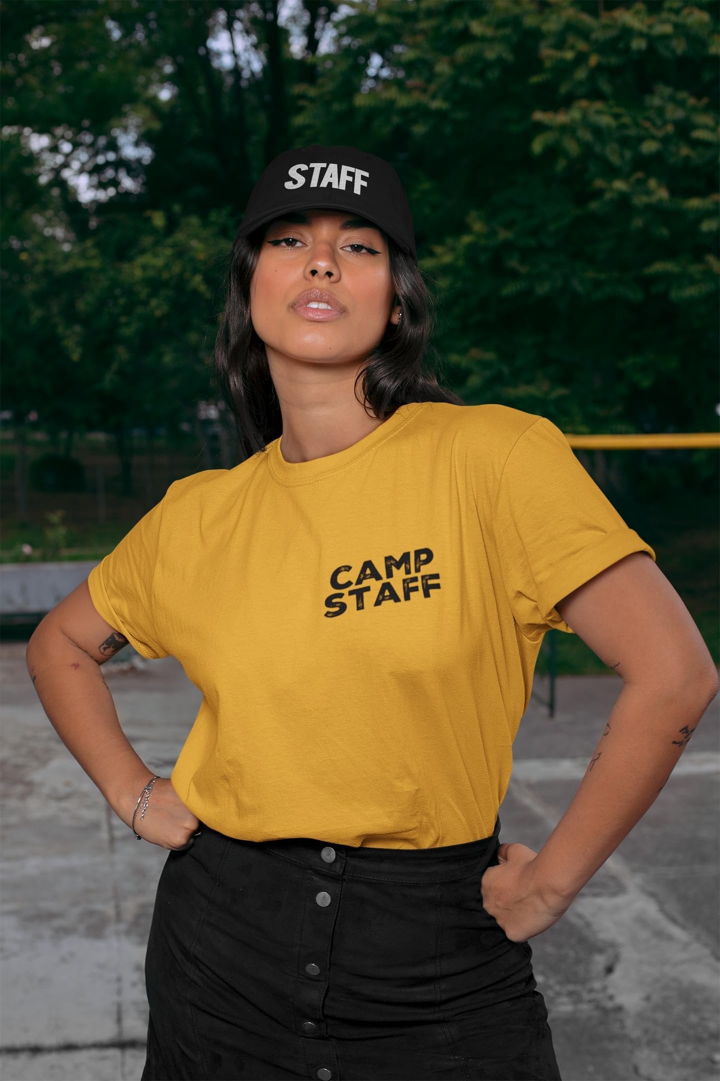 Person wearing a yellow 'Camp Staff' t-shirt and black 'Staff' cap outdoors.