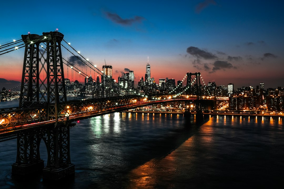 The Williamsburg Bridge illuminated at night with the New York City skyline behind